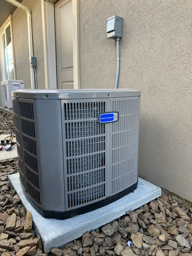 An American Standard air conditioner condenser on a concrete pad in a river-rock bed