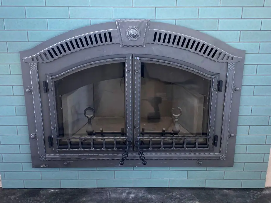 An arched wrought-iron gas fireplace front set into a teal tile surround