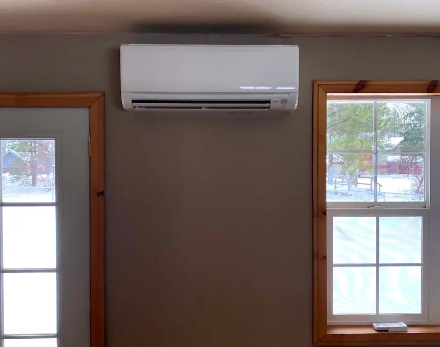 A Mitsubishi ductless wall unit mounted above a door with snow visible through the windows