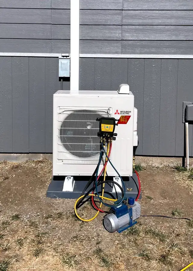 A Mitsubishi outdoor unit on a pad with manifold gauges and a vacuum pump connected during commissioning
