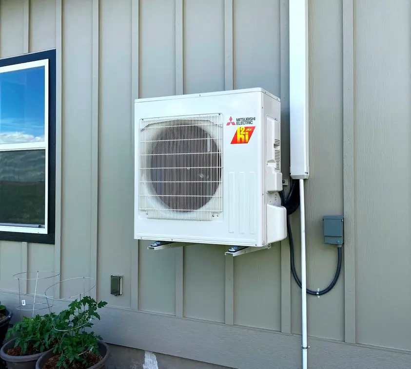 A Mitsubishi Hyper-Heat outdoor unit mounted on wall brackets against siding